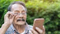 Close up of elder gray beard white hair with glasses looking attention at his smartphone to reading news at garden alone