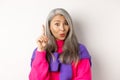 Close up of elderly asian woman in stylish hipster clothes, raising finger and saying idea, have suggestion, standing Royalty Free Stock Photo