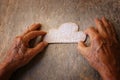 A close up of an elderly man holding a paper cloud on a wooden table. Concept of thinking about childhood dreams, sadness and lone