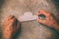 A close up of an elderly man holding a paper cloud on a wooden table. Concept of thinking about childhood dreams, sadness and lone