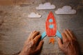 A close up of an elderly man holding a paper rocket on a wooden table. Concept of thinking about childhood dreams, sadness and lon