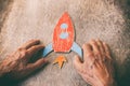 A close up of an elderly man holding a paper rocket on a wooden table. Concept of thinking about childhood dreams, sadness and lon