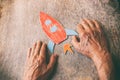 A close up of an elderly man holding a paper rocket on a wooden table. Concept of thinking about childhood dreams, sadness and lon