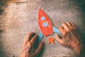 A close up of an elderly man holding a paper rocket on a wooden table. Concept of thinking about childhood dreams, sadness and lon