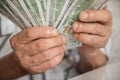 Close-up of an elderly man`s hands holding 100 dollar bills in front of him. Pension payments to an elderly man. Home budget for Royalty Free Stock Photo