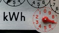 A close-up of an electricity meter kWh symbol and red numbered dial.