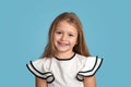 Close up emotional portrait of young blonde smiling girl wearing white blous with black strips on blue background in studio Royalty Free Stock Photo