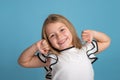 Close up emotional portrait of young blonde smiling girl wearing white blous with black strips on blue background in studio. She Royalty Free Stock Photo