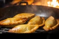 Close-up of empanadas being fried in a pan, showing off their crispy and golden exterior with steam rising from the hot oil