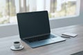 Close up of empty laptop on wooden desktop with coffee cup, notepad, pen, mock up place on screen, blurry office interior with Royalty Free Stock Photo