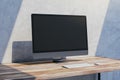 Close up of empty mock up computer screen on wooden desktop and concrete wall background with shadow. Designer desktop and ad Royalty Free Stock Photo