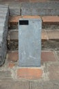 Close up of blank outdoor single gray stone pillar cement signpost on old brick floor with black small plate at corner of board