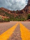 Close-up of empty pawed road with two yellow lines with red mountains on the background, Zion national park