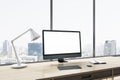 Close up of empty white computer monitor on wooden office desktop with objects, lamp and supplies on panoramic window and city Royalty Free Stock Photo