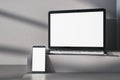 Close up of empty white laptop computer and phone on gray desk. Concrete wall background, shadows and pedestal or podium. Device Royalty Free Stock Photo