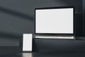 Close up of empty white laptop and phone on dark gray desk. Concrete wall background, shadows and pedestal or podium. Device Royalty Free Stock Photo
