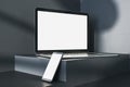 Close up of empty white laptop and smartphone on dark gray desk. Concrete wall background, shadows and pedestal or podium. Device Royalty Free Stock Photo