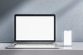 Close up of empty white laptop and smartphone on gray desk. Concrete wall background. Device presentation and online education Royalty Free Stock Photo