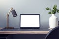 Close up of empty white laptop on wooden desk with decorative vase and plant, lamp and mock up place on concrete wall background. Royalty Free Stock Photo
