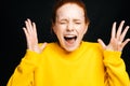 Close-up of excited angry young woman screaming with closed eyes on isolated black background.