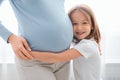 Excited little girl embracing her pregnant mother tummy Royalty Free Stock Photo