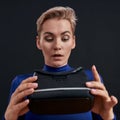 Close up of excited woman with short hair in turtleneck looking at virtual reality headset, vr glasses, holding it Royalty Free Stock Photo