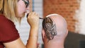 A close-up, the execution of a master, an artist mehendi, a tattoo, a picture of henna on white skin scalp, a bald Royalty Free Stock Photo