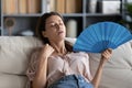 Close up exhausted overheated woman waving paper fan at home