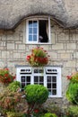 A close up of an exterior of an old thatched cottage with hanging baskets and flowers in front Royalty Free Stock Photo