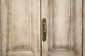 Close up exterior view of an ancient wooden garage door. Metallic elements, handle and keyhole are visible. White and grey painted