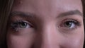 Close-up eye-portrait of young brunette caucasian girl watching gladly into camera on black background.