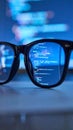 Close up of eyeglasses reflecting glowing computer code on a dark screen Royalty Free Stock Photo