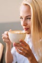 Close-up face of attractive young blonde woman drinking coffee hot cappuccino coffee with beautiful pattern sitting in