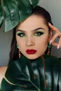 Close up face of beautiful young woman covering by green monstera green palm. Portrait of beauty woman with makeup red lips clear Royalty Free Stock Photo