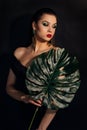 Close up face of beautiful young woman covering by green monstera green palm. Portrait of beauty woman with makeup red lips clear Royalty Free Stock Photo