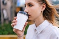 Close-up face of charming young woman enjoying delicious takeaway coffee on city street in summer day. Stylish female Royalty Free Stock Photo