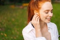Close-up face of cheerful redhead young woman wearing wireless earphones outdoors, Royalty Free Stock Photo