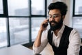 Close-up face of cheerful young Indian businessman in glasses making business call talking on smartphone in office Royalty Free Stock Photo
