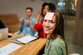 Close-up face of cheerful young woman playing guessing game with sticky notes on forehead after work for entertainment Royalty Free Stock Photo