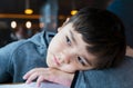 Close up face of cute little child boy lying head on hands, Candid shot mixed race kid sitting alone with smiling face looking