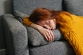 Close-up face of exhausted young woman sleeping on cozy couch in living room, lying on stomach. Tired redhead female Royalty Free Stock Photo