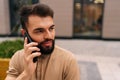 Close-up face of handsome young man talking on mobile phone sitting on bench on city street on background of building Royalty Free Stock Photo