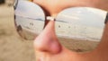 Close-up face of a happy woman in sunglasses. The beach with the resting people is reflected in the glasses. Royalty Free Stock Photo
