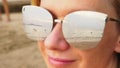 Close-up face of a happy woman in sunglasses. The beach with the resting people is reflected in the glasses. Royalty Free Stock Photo