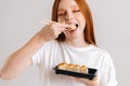 Close-up face of happy young woman with closed eyes eating delicious sushi rolls with chopsticks standing on white Royalty Free Stock Photo