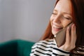 Close-up face of laughing young woman talking on smartphone at home. Cheerful redhead female making answering call by Royalty Free Stock Photo