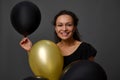 Close-up face portrait of African woman with beautiful smile posing with black and gold air balloons against gray background with Royalty Free Stock Photo