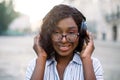 Close up face portrait of pretty smiling young african lady, listening to music on headphones, enjoying walk outdoors on Royalty Free Stock Photo