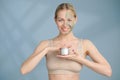 A close-up face portrait of a young blonde woman. Green beauty mask on half of the face. A woman holds a jar of Royalty Free Stock Photo