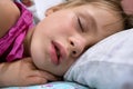 Close up of a face of pretty little child girl with slightly open mouth and scattered around hair sleeping in bed at home